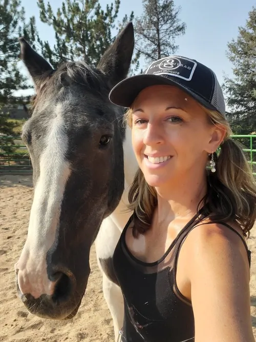 Melissa Clark, LCSW, smiling beside Patches, a dark horse with a white blaze