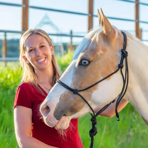 Melissa Clark smiling beside a palomino paint horse in a rope halter